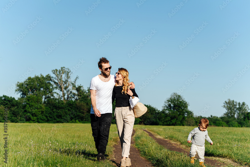 Spouses hug-walking in a countryside, their son running along. Spouses hug-walking in a countryside, their son running along.
