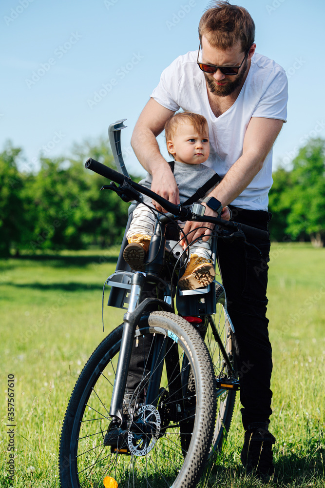 Young bearded man keen on strapping his kid to bike baby chair Young bearded man keen on strapping his kid to bike baby chair