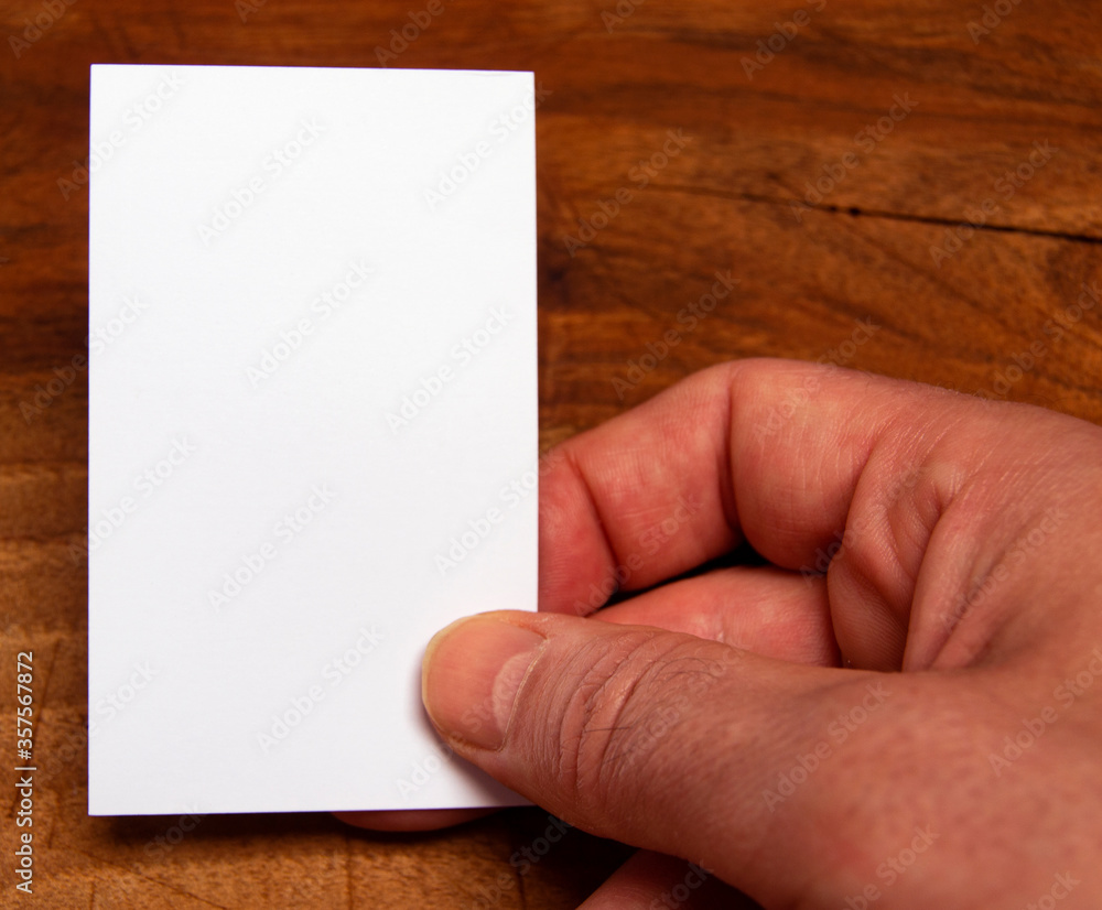 Obraz premium white empty card in male caucasian hand on a wooden background
