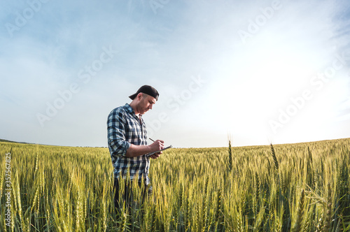 male agronomist in cap takes notes in a notebook on a green agricultural field of wheat © Taras Rudenko
