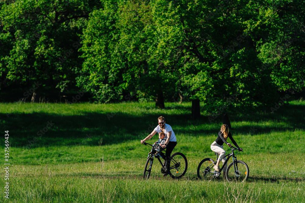 Family biking in a countryside, along trees and fields, turning 180
