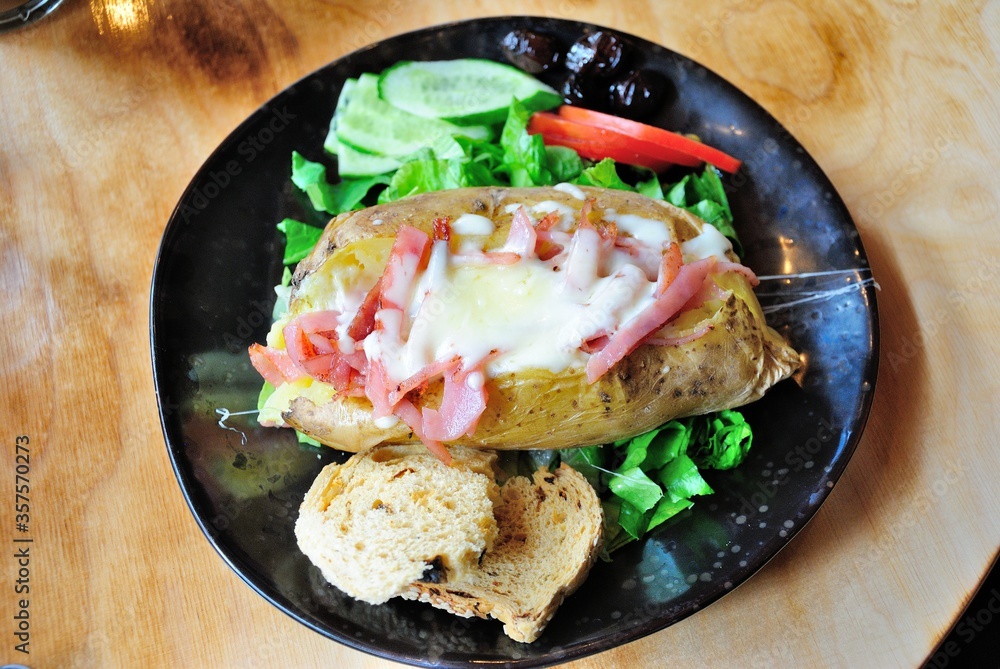 A baked (jacked) potato with cheese and bacon, served on a plate with lettuce, cucumber, tomato and a piece of bread in Cyprus A baked (jacked) potato with cheese and bacon, served on a plate with lettuce, cucumber, tomato and a piece of bread in Cyprus