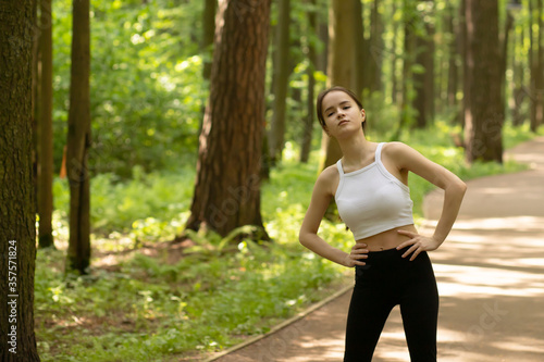 Sport, diet, healthy lifestyle. Girl warming up in the park before jogging, doing exercises in nature