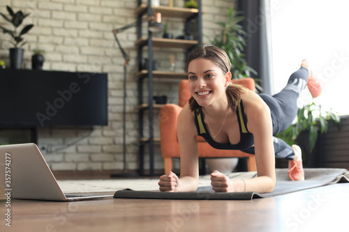 Beautiful fitness woman doing a plank exercise watching online tutorials on laptop, training in living room. Healthy lifestyle. Girl goes in for sports at home.