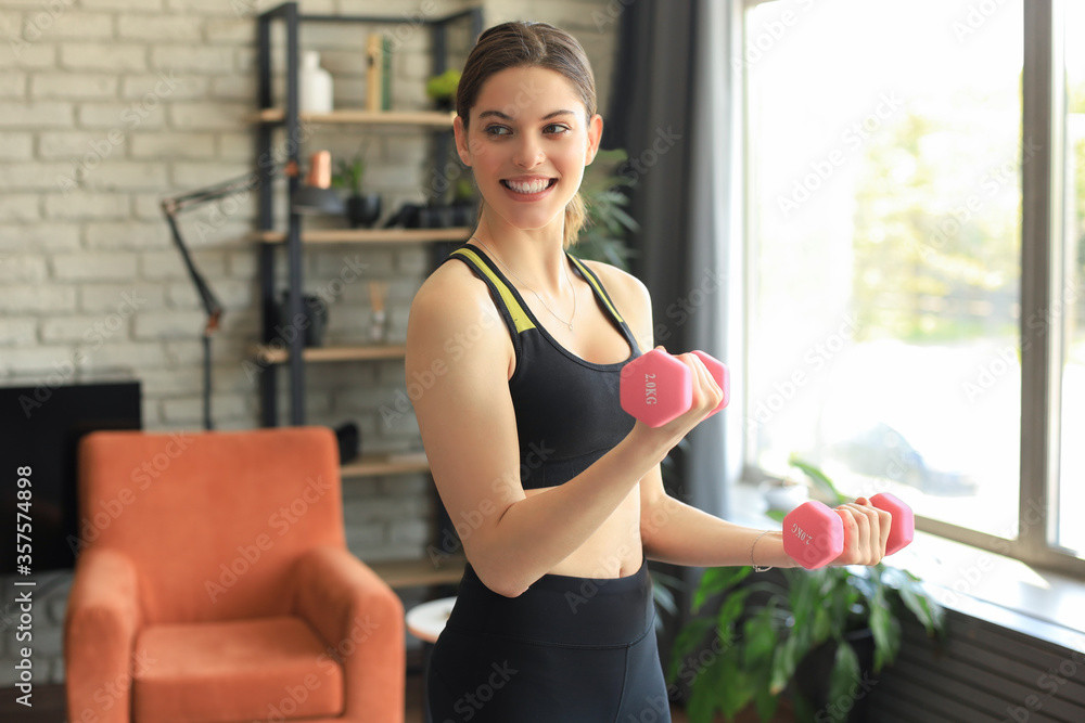 Young beautiful sports girl in leggings and a top does exercises with dumbbells. Healthy lifestyle. A woman goes in for sports at home.
