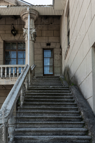 An old building with columns and stucco. Wide staircases lead to the second floor. Strict geometry. Summer. High quality photo