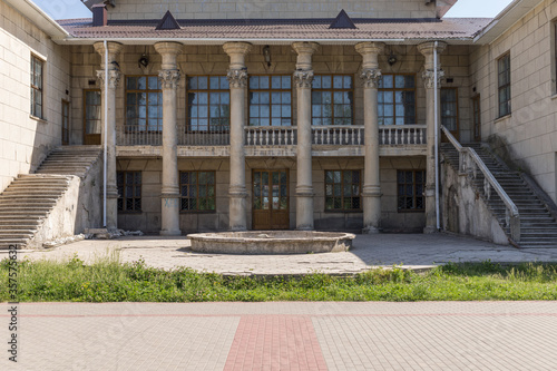 An old building with columns and stucco. Wide staircases lead to the second floor. Strict geometry. Summer. High quality photo