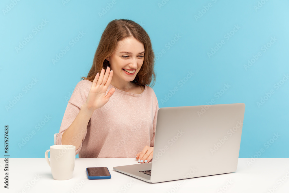 Φωτογραφία Hi! Beautiful woman waving hand gesturing hello to laptop screen, talking on video call with friend, communicating online conference at home office