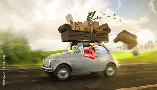 Umzug - Frau im Kleinwagen transportiert Sofa und Hausrat auf ihrem Dach