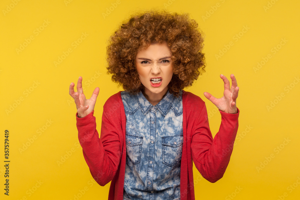 Aggressive emotions. Portrait of crazy irritated woman with curly hair in casual outfit raising fist frustrated and furious, expressing anger, hate and rage. studio shot isolated on yellow background Aggressive emotions. Portrait of crazy irritated woman with curly hair in casual outfit raising fist frustrated and furious, expressing anger, hate and rage. studio shot isolated on yellow background