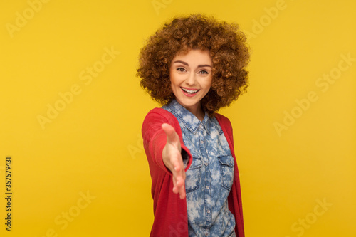 Welcome, nice to meet you! Portrait of amiable kind woman with fluffy curly hair in casual outfit giving hand to handshake, smiling with hospitable friendly expression. indoor studio shot isolated