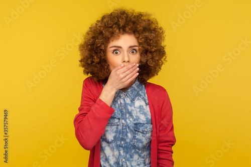I'm scared to talk! Portrait of shocked terrified woman with curly hair closing her mouth and looking frightened, intimidated victim afraid to say secret. studio shot isolated on yellow background