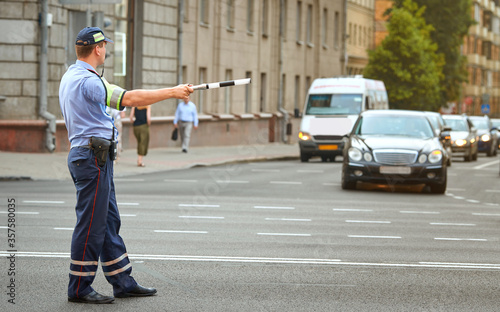 Police officer directing traffic in the city with police stick. Traffic police adjusts cars at the intersection of  avenue, rush hour. Policeman regulating traffic