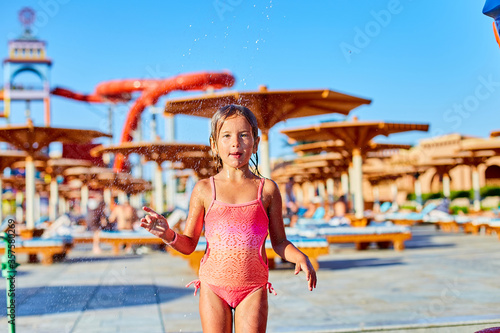 Funny little girl in swimsuit cooling in shower outside