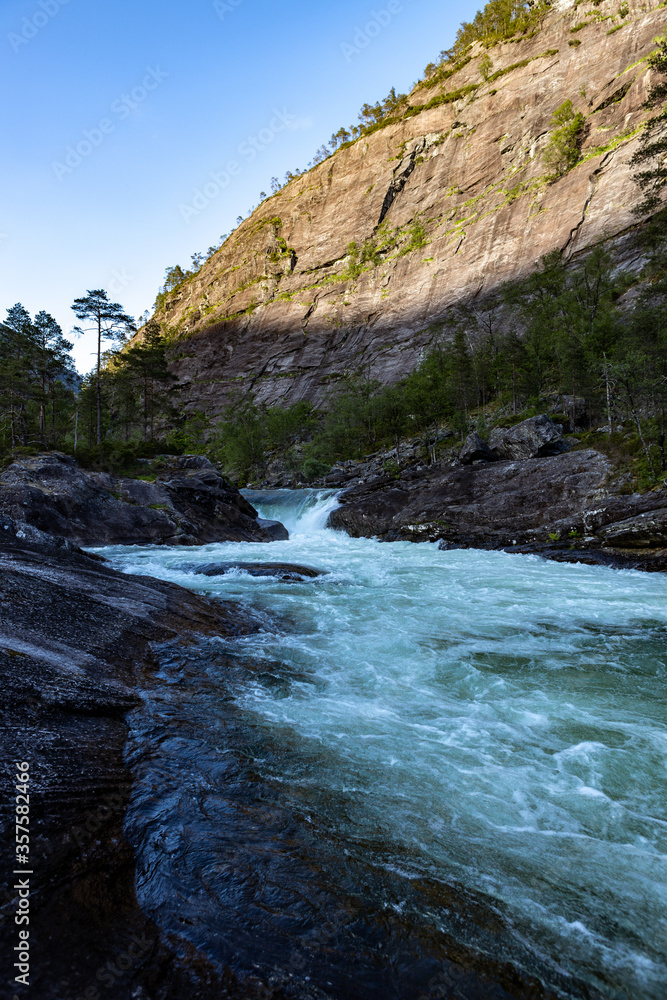 Obraz premium Waterfall in Norway with sun on a mountain in the background portrait