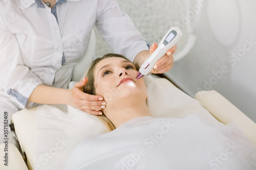 Cropped image of female surgeon beautician removing pigmentation and vascular nets on the skin of the patient  beautiful young woman  using laser tool. Laser cosmetology