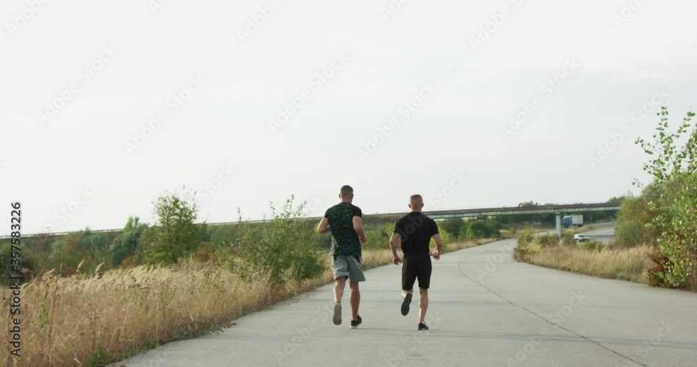 Back view of two sportsmen jogging into the distance on a path among nature Back view of two sportsmen jogging into the distance on a path among nature
