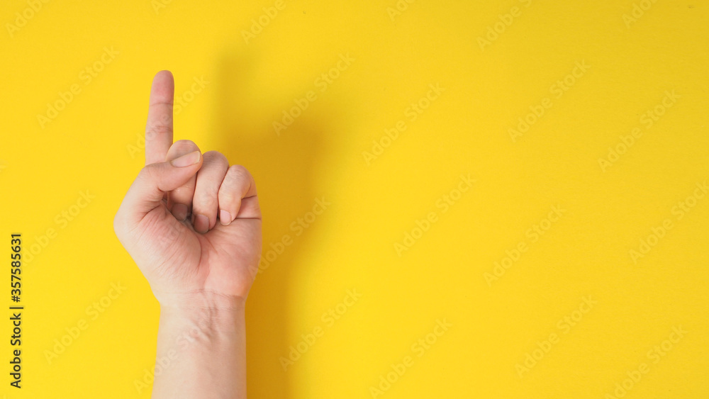 Male model is doing one finger or point up hand sign on yellow background. - obrazy, fototapety, plakaty 