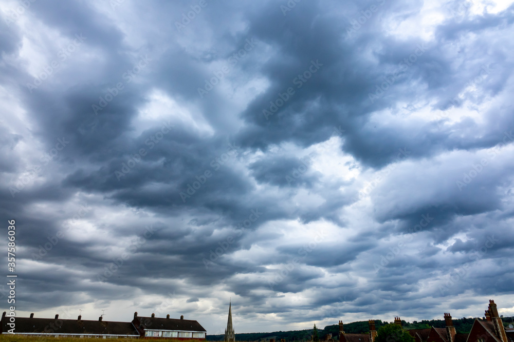 Wide view of dark moody clouds over town skyline with church spire