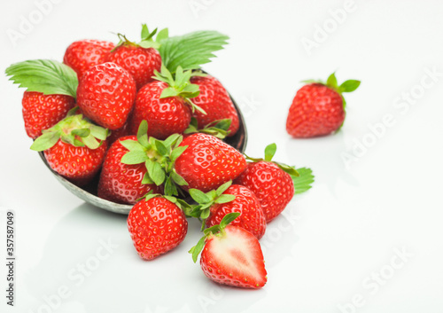 Fresh raw organic strawberries in steel bowl plate on white background with berries next to it.
