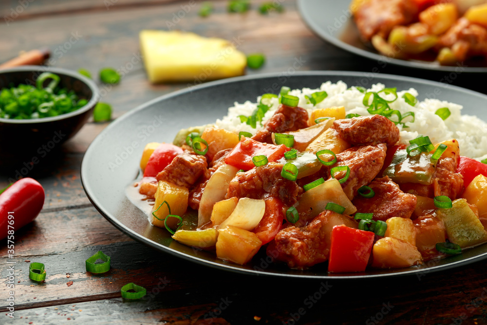 Pineapple and Chicken in sweet and sour sauce with bell pepper, rice and spring onion in black plate Pineapple and Chicken in sweet and sour sauce with bell pepper, rice and spring onion in black plate