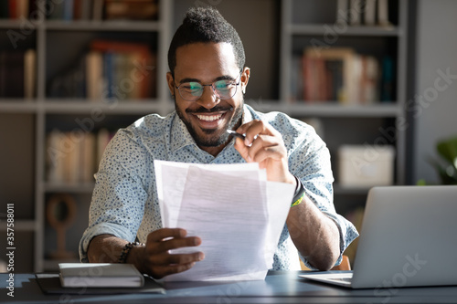 African student guy sitting at desk holding papers printed tasks perform test prepares for entrance exams enjoy process of study. Teacher checking assignment homework, company lawyer paperwork concept photo