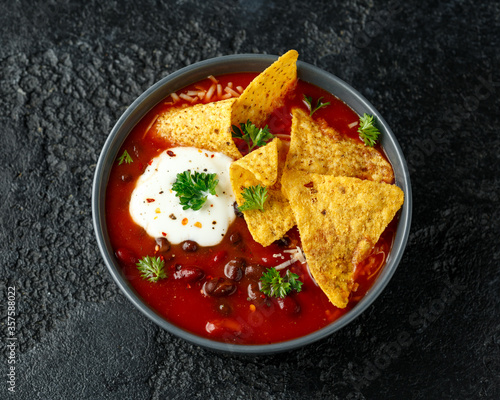 Mexican Chilli bean soup with yogurt, cheese and tortilla chips in black bowl