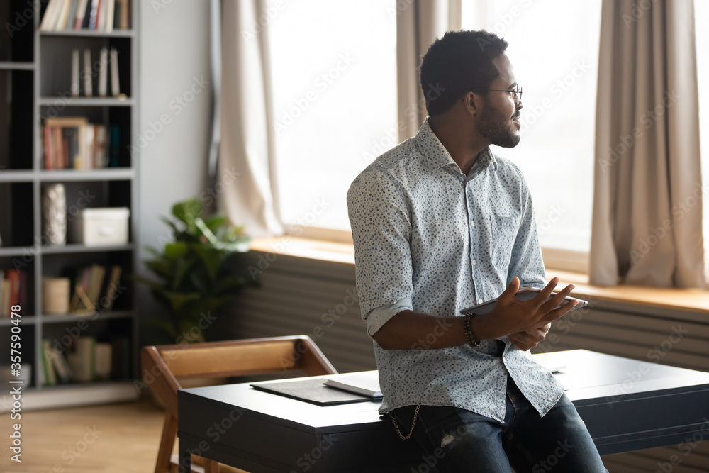 African guy holding tablet distracted from modern wireless device usage looking out the window thinking feels confident and tranquil. Freelancer businessman take break enjoy daydreaming indoor concept African guy holding tablet distracted from modern wireless device usage looking out the window thinking feels confident and tranquil. Freelancer businessman take break enjoy daydreaming indoor concept