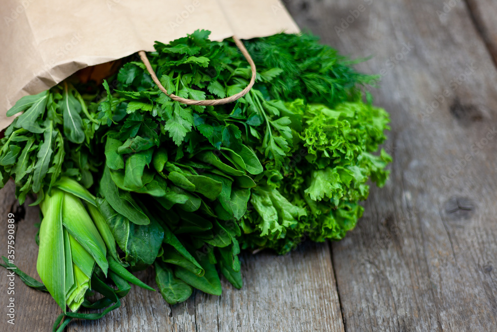 Fresh greens in a paper bag - green onions, dill, parsley, spinach, arugula, sorrel. Home delivery of food and fresh vegetables. Wooden background with place for text. Packaging and cooking. Fresh greens in a paper bag - green onions, dill, parsley, spinach, arugula, sorrel. Home delivery of food and fresh vegetables. Wooden background with place for text. Packaging and cooking.
