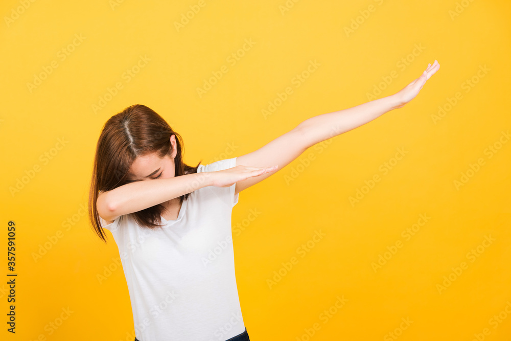 Asian happy portrait beautiful cute young woman teen smile standing wear t-shirt move showing DAB dance against gesture isolated, studio shot on yellow background with copy space Asian happy portrait beautiful cute young woman teen smile standing wear t-shirt move showing DAB dance against gesture isolated, studio shot on yellow background with copy space