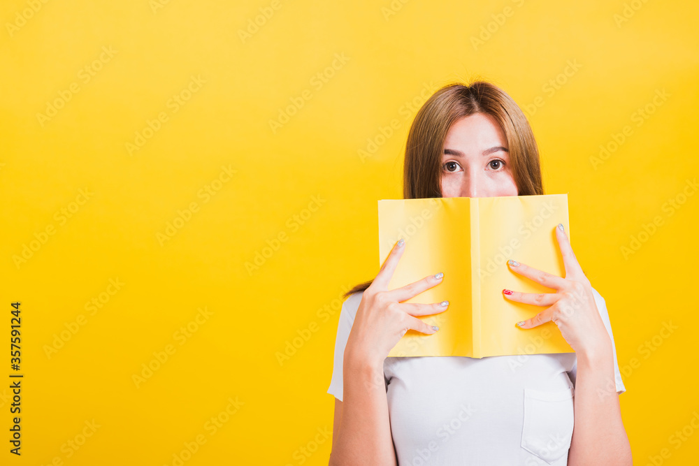 Portrait Asian Thai beautiful happy young lifestyle woman stands holding yellow book or diary her looking to camera, studio shot isolated on yellow background, with copy space Portrait Asian Thai beautiful happy young lifestyle woman stands holding yellow book or diary her looking to camera, studio shot isolated on yellow background, with copy space