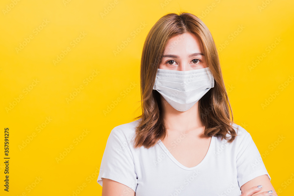 Portrait Asian beautiful young woman stand crossed arm wearing face mask protection filter dust pm2.5 anti-pollution, anti-smog, air pollution and COVID virus on a yellow background, with copy space Portrait Asian beautiful young woman stand crossed arm wearing face mask protection filter dust pm2.5 anti-pollution, anti-smog, air pollution and COVID virus on a yellow background, with copy space