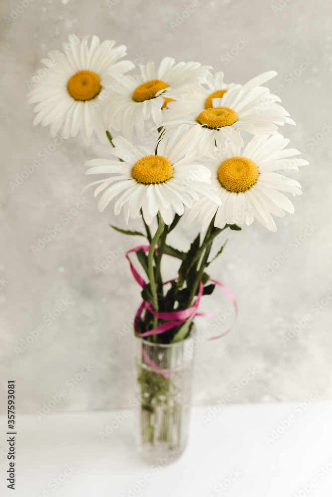Bouquet of daisy flowers in a vase on a gray background.
