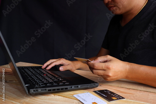 A man wearing a shirt sitting at a desk and thinking of ordering products online, on the other hand, holding a credit card and the other hand pressing the notebook's keyboard. photo