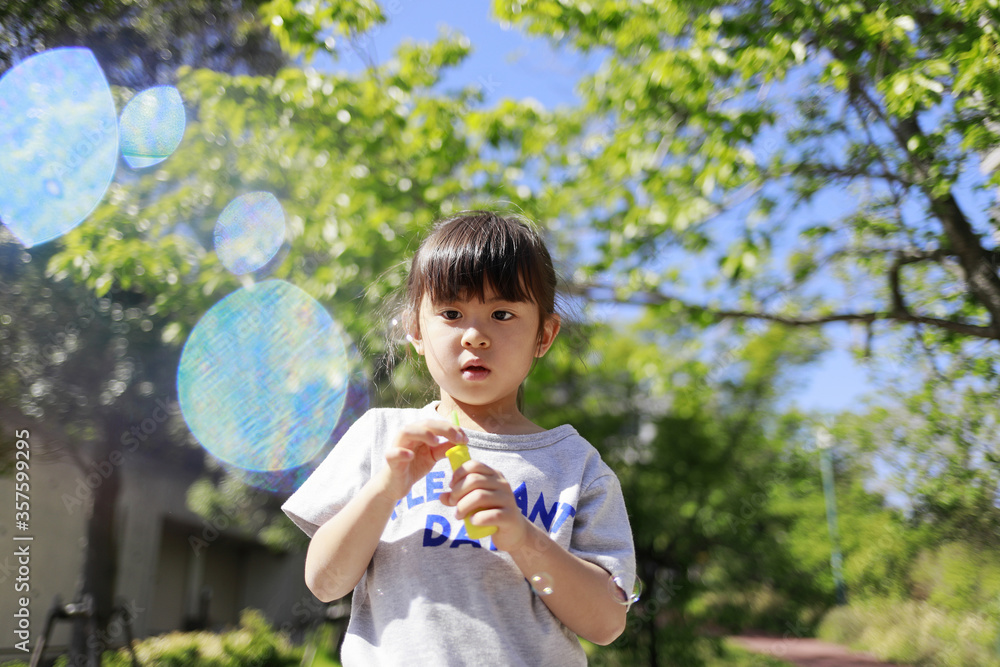 緑の中でシャボン玉で遊ぶ幼児(5歳児)