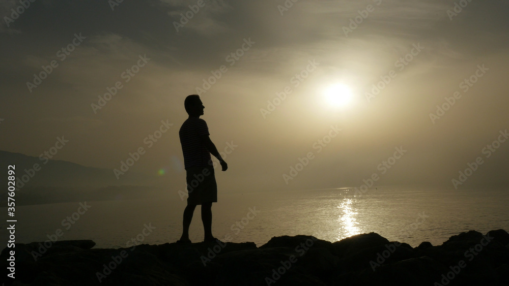 Silhouette of young man standing on seashore and admires sunrise over sea water in Marbella area, Spain
