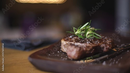 Meat steak. Meat and rosemary. A close up of a steak with sea salt and herbs. Steak on a wooden board in a restaurant.  Serving a steak at a meat restaurant.