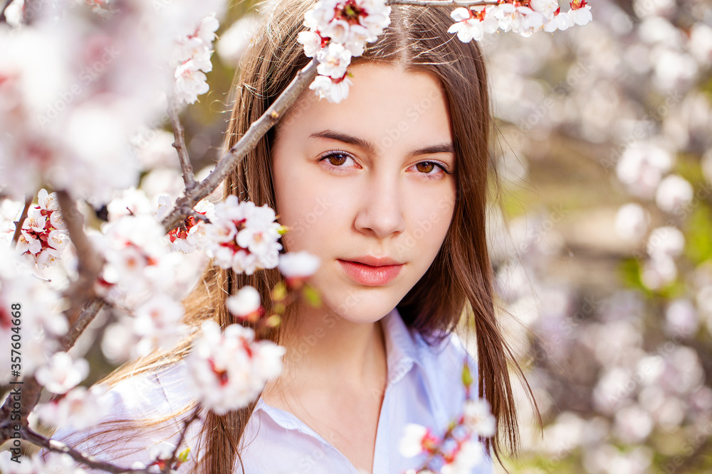 Fototapeta premium Pretty teen girl are posing in garden near blossom cherry tree with white flowers