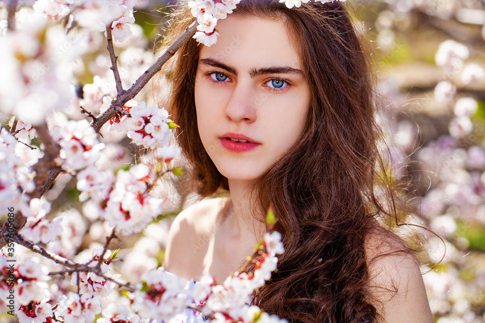 Fototapeta premium Pretty teen girl are posing in garden near blossom cherry tree with white flowers