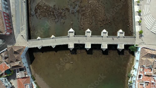 Aerial top view of people walking on an old Roman Bridge, in Tavira city, Algarve, Portugal. Gilao river at low tide.
