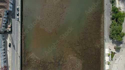 Aerial Top view over Gilao River at low tide, in Tavira City, Algarve, Portugal. People walking on an Old Roman Bridge. Drone forward movement