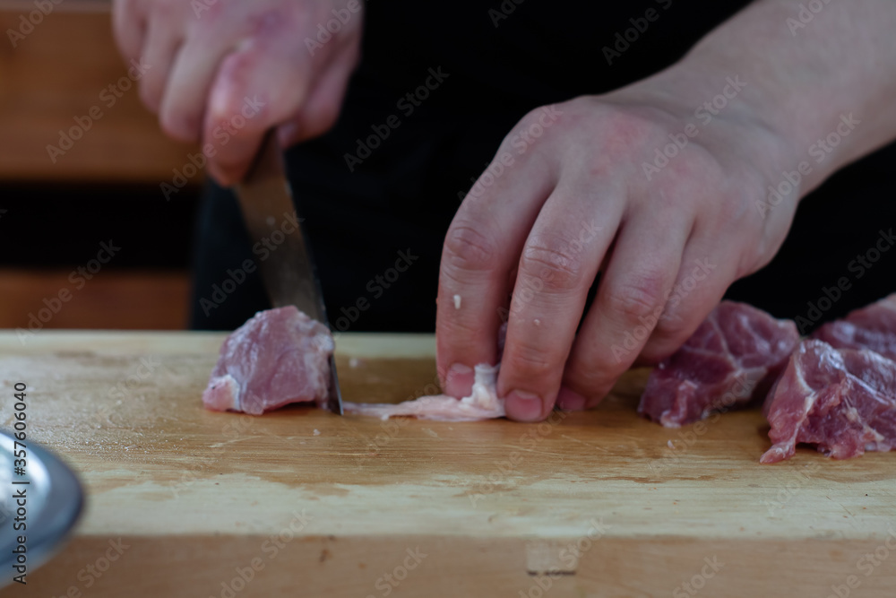 cutting meat into pieces with a knife on a wooden Board. the cook cuts the meat.