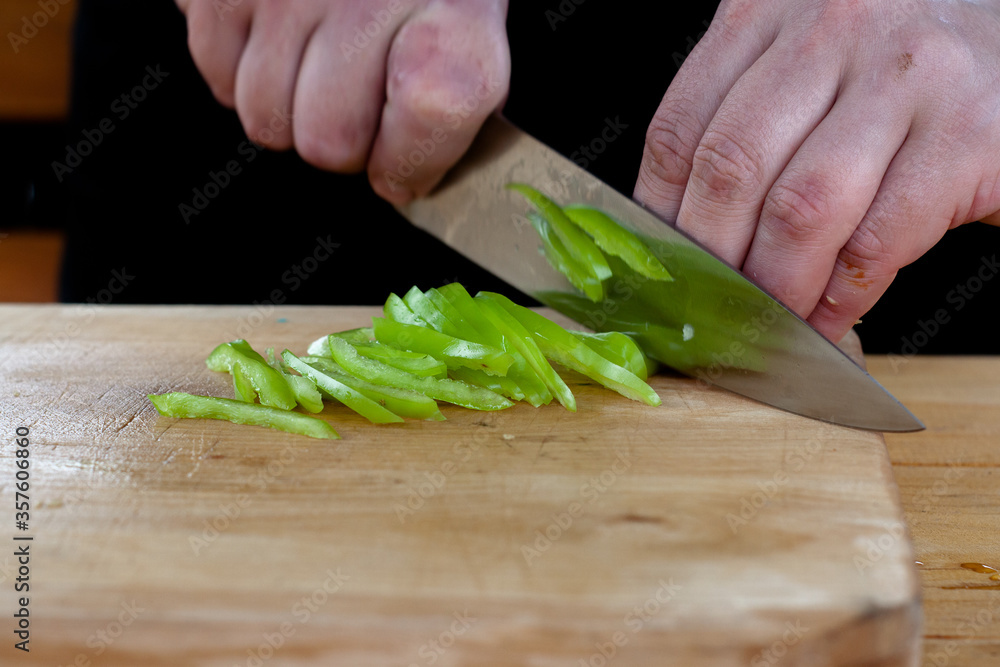 the cook cuts green peppers into strips on a wooden Board the cook cuts green peppers into strips on a wooden Board