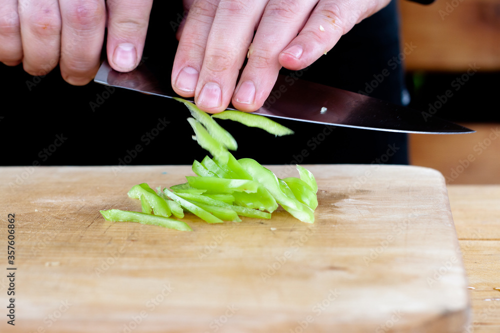 the cook cuts green peppers into strips on a wooden Board the cook cuts green peppers into strips on a wooden Board
