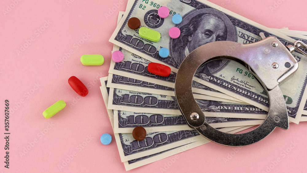 metal handcuffs with money and pills on a pink background