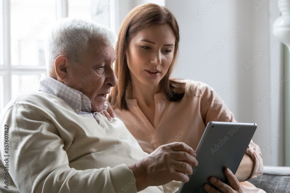 Caring grownup daughter teaching older father to use computer tablet close up, pointing at screen, mature man asking questions about mobile device to young woman, elderly and technology concept Caring grownup daughter teaching older father to use computer tablet close up, pointing at screen, mature man asking questions about mobile device to young woman, elderly and technology concept