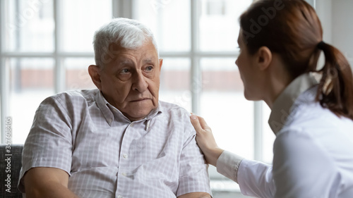 Female doctor comforting upset older patient at meeting  touching shoulder  expressing empathy and support  sad unhappy lonely mature man looking at caregiver close up  elderly healthcare concept