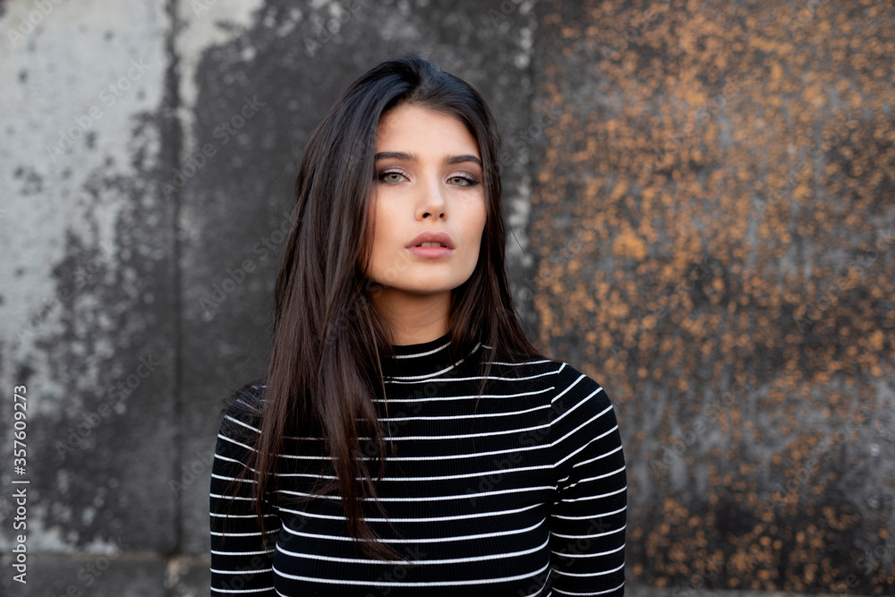 Frontal portrait of a graceful girl with brunette hair, in casual clothes, with makeup, supported by a black wall. Frontal portrait of a graceful girl with brunette hair, in casual clothes, with makeup, supported by a black wall.
