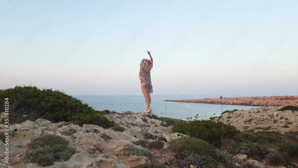 Vacation. Young slim woman sport body in bikini and pareo walking on rocky terrain on a background of blue sea at Cape Greco for sunset Vacation. Young slim woman sport body in bikini and pareo walking on rocky terrain on a background of blue sea at Cape Greco for sunset