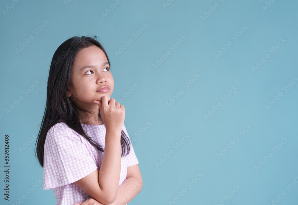 Asian little girl standing thinking on blue background isolated Asian little girl standing thinking on blue background isolated